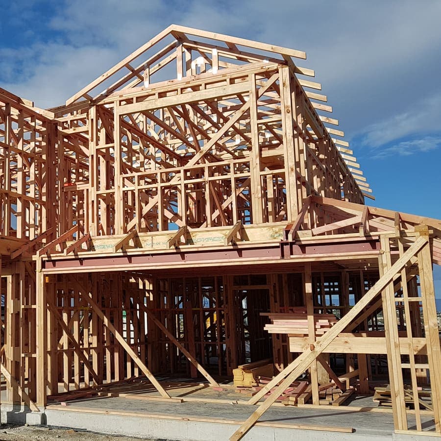 Rangka kayu rumah dua lantai yang sedang dibangun dengan latar langit biru