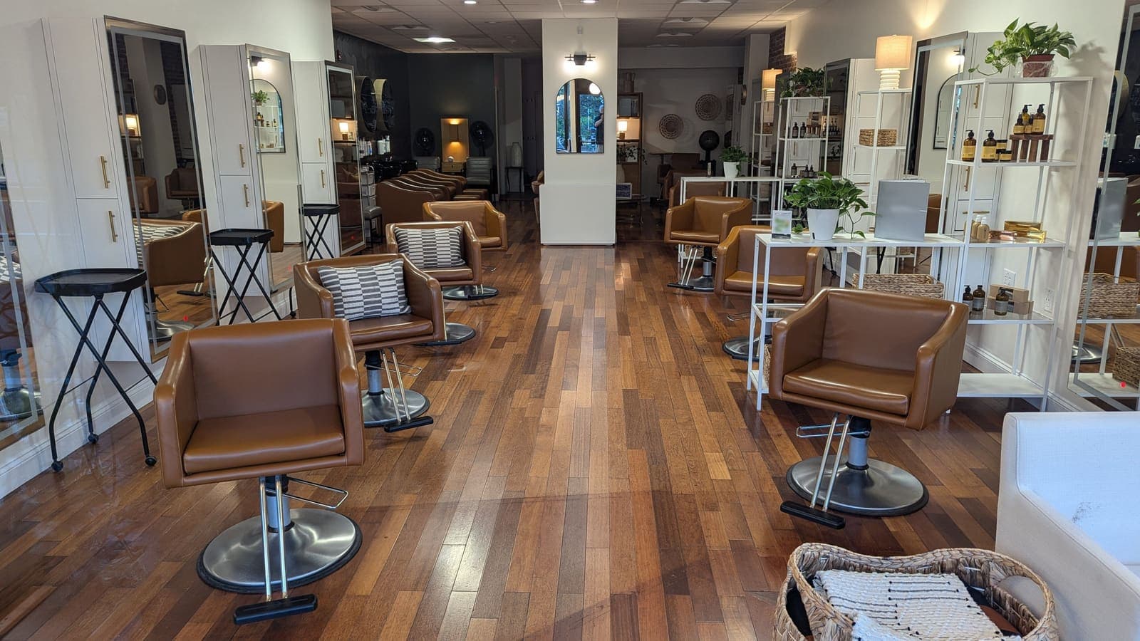 Ruang salon yang terang dengan deretan kursi kulit cokelat, cermin tinggi, rak produk perawatan, dan lantai kayu