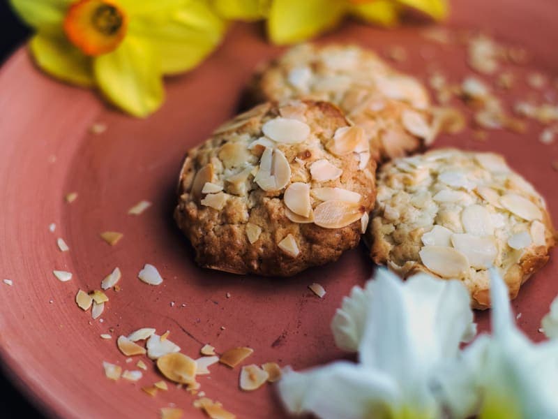 Kue kering almond di atas piring tanah liat dengan bunga di sampingnya